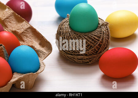 Easter composition. Multi-colored eggs in a box, in a nest of hemp threads, on a white table.` Stock Photo